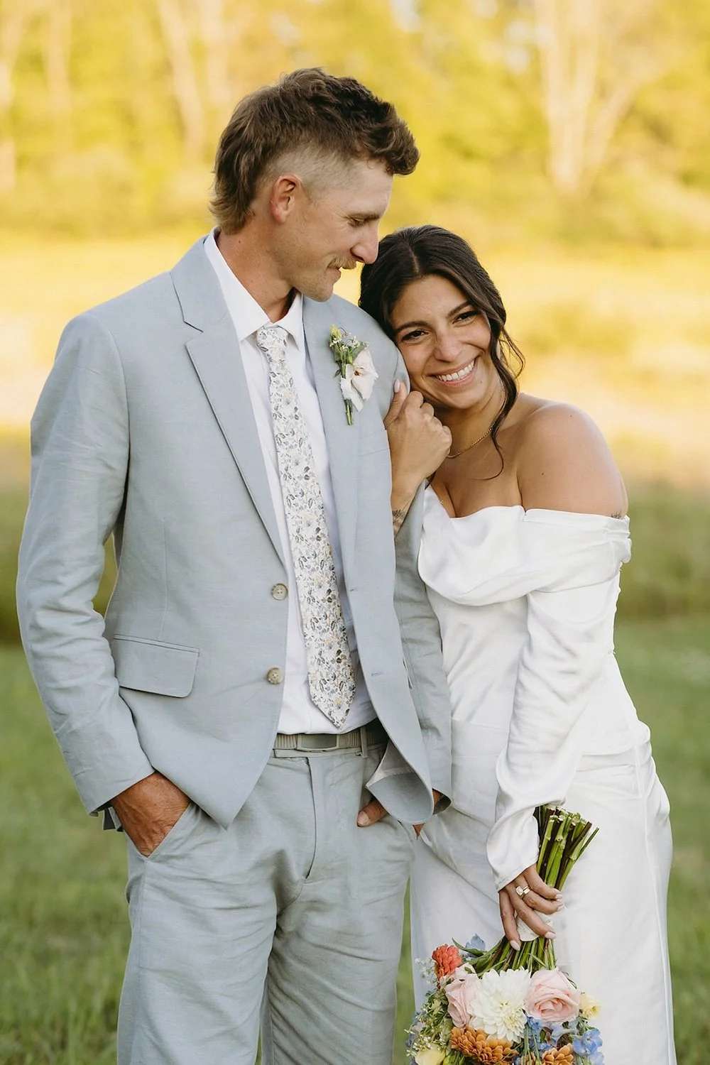 The bride holds her grooms arm as she rests her head on his shoulder smiling.