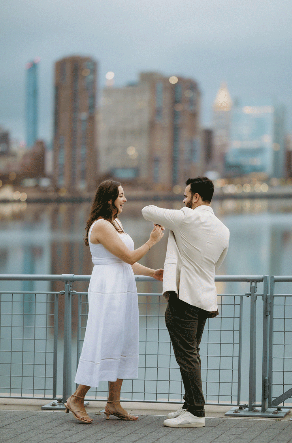 The couple shares a dance infront of the water with the cityscape as their background.