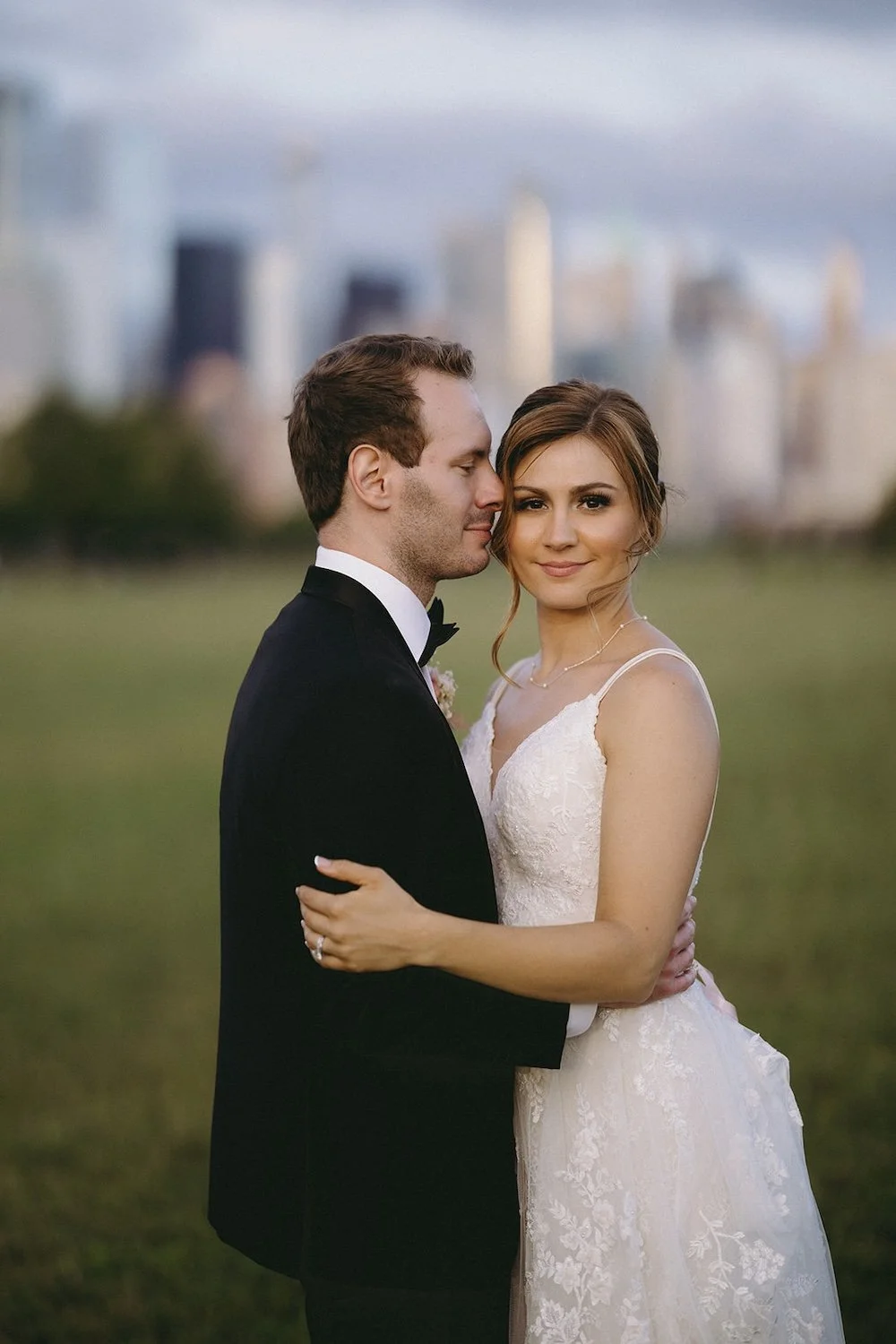 The groom looks at his bride as she looks toward the camera. The city scape blurred in the background.
