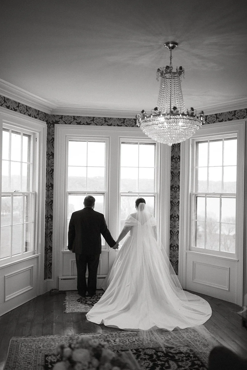 Black and white photo of the bride and groom holding hands while admiring the lake view from the bridal suite.
