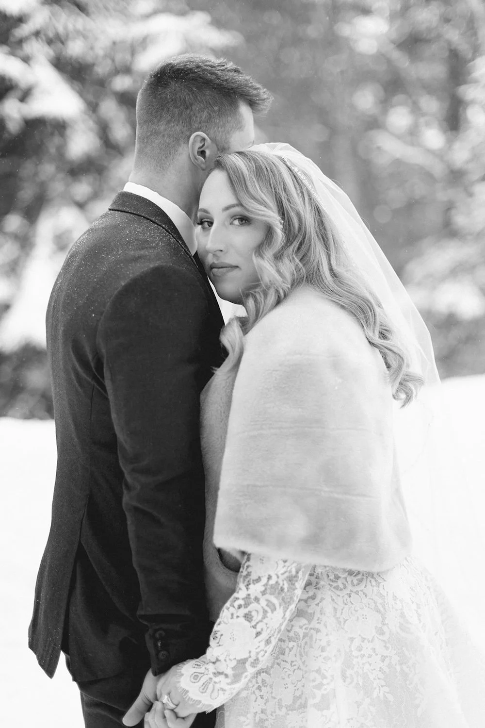 Black and white photo of the bride staring into the camera as she holds her groom close.