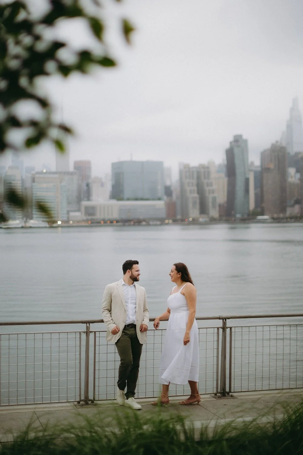 The couple rest against the railing of the boardwalk with the city as their background.