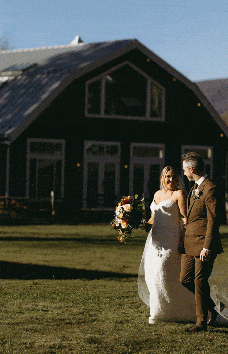The bride and groom walk hand in hand outside the venue while sharing a smile.