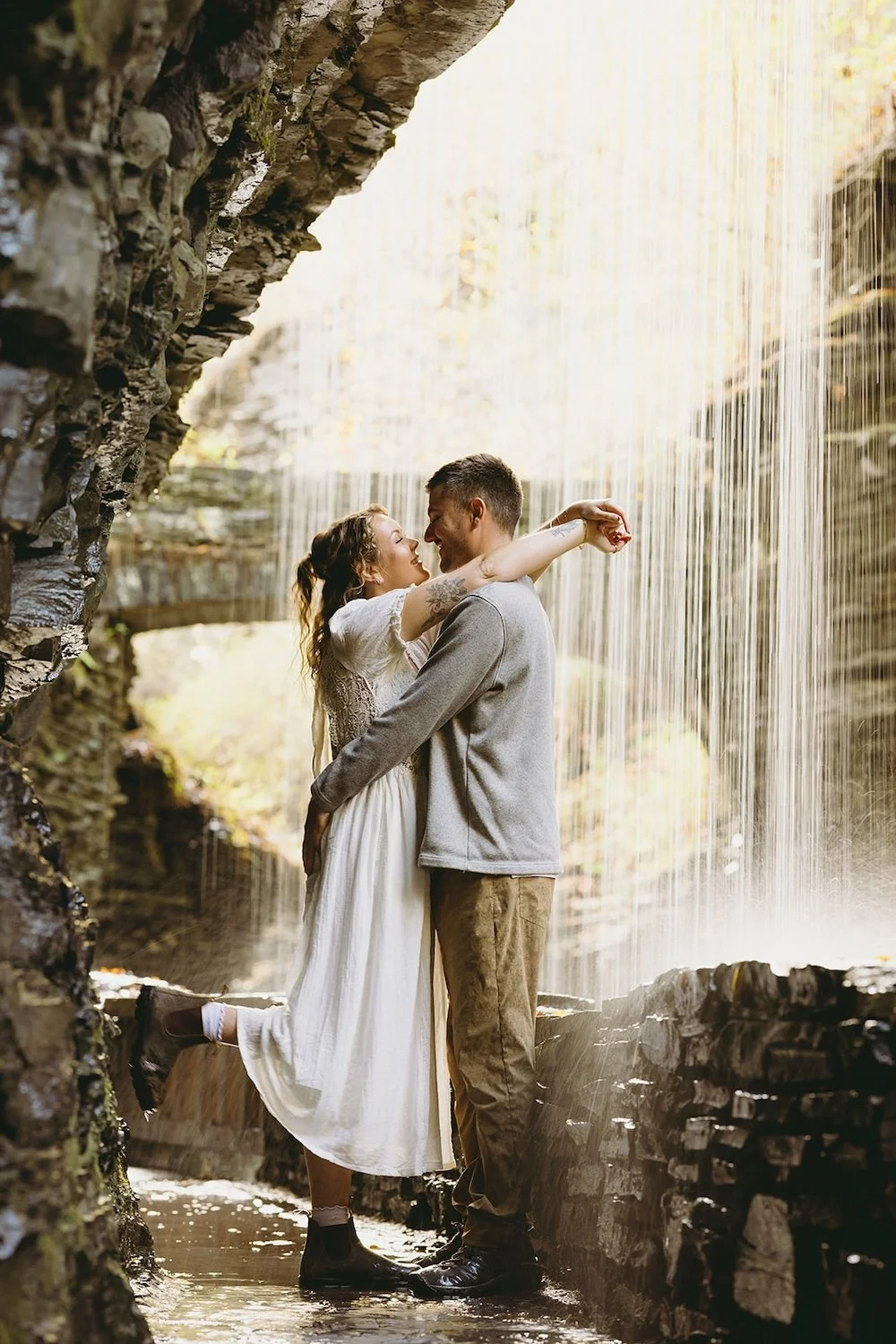 The engaged couple stand in the gorge with the waterfall surrounding them.