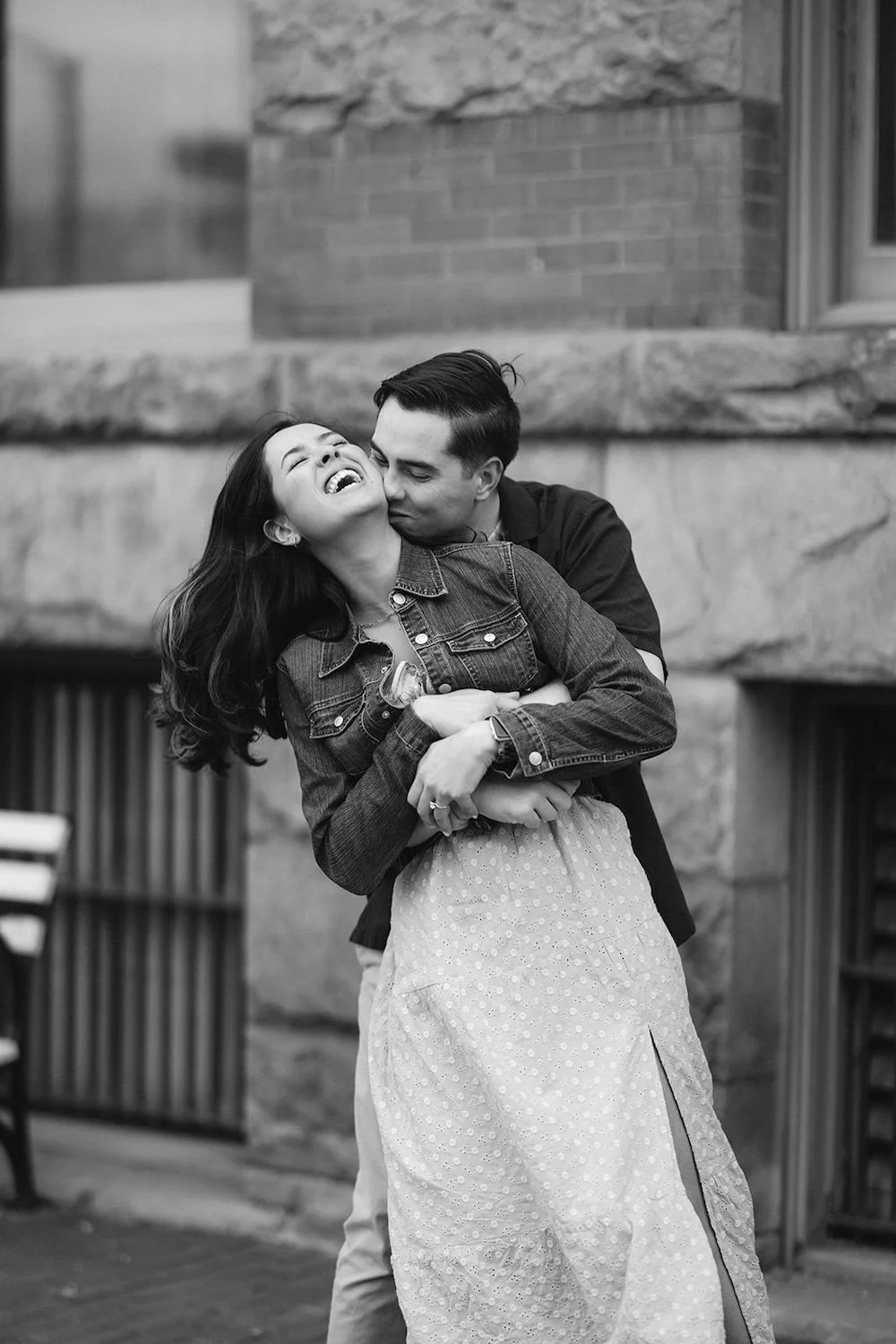 The future groom has his arms wrapped around the bride as he reaches in for a kiss to the neck.