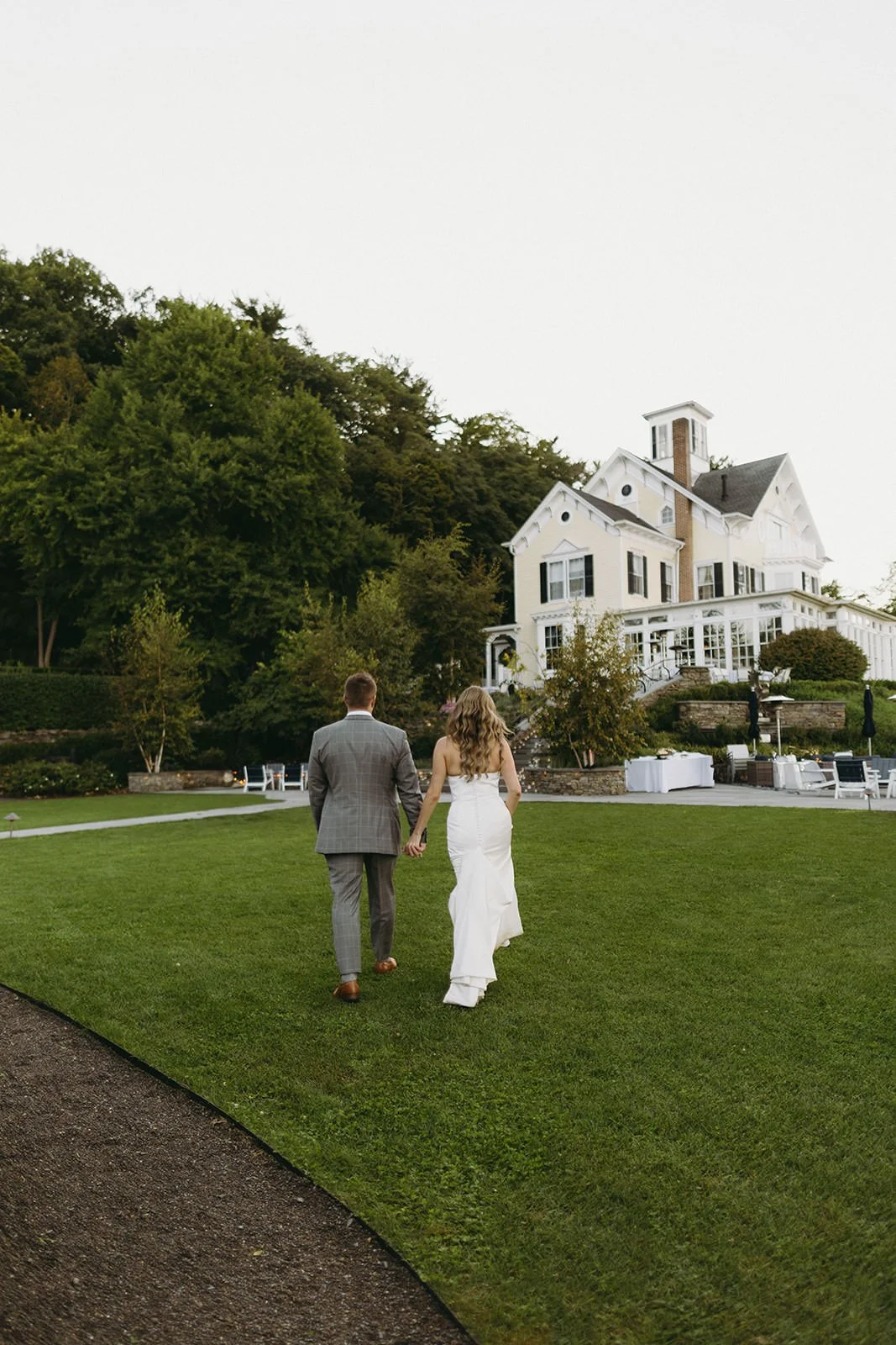 Bride and groom walking hand in hand toward an elegant estate wedding venue, classic outdoor wedding photography.