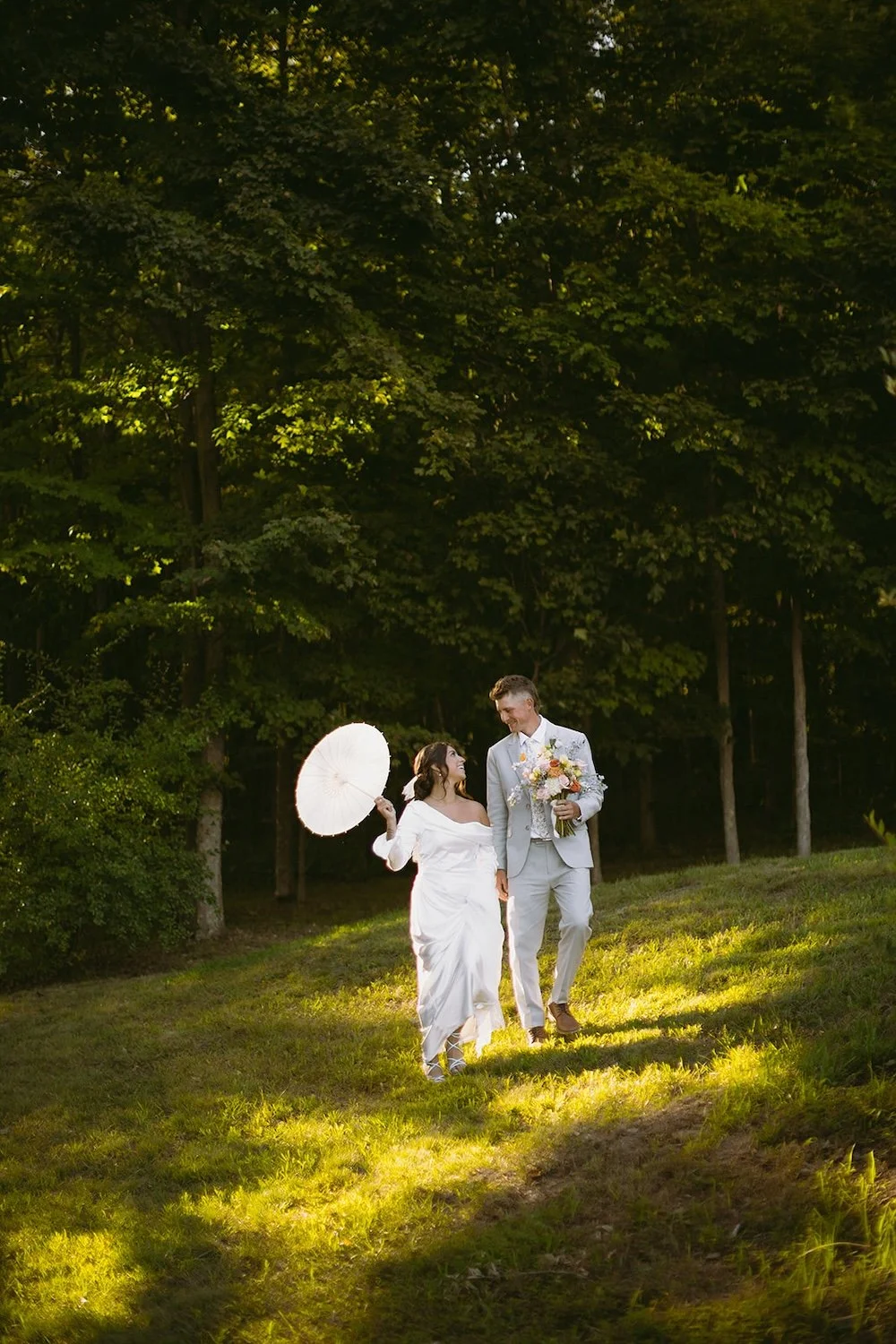 The happy couple walk the hillside with the sunlight beaming down on them.