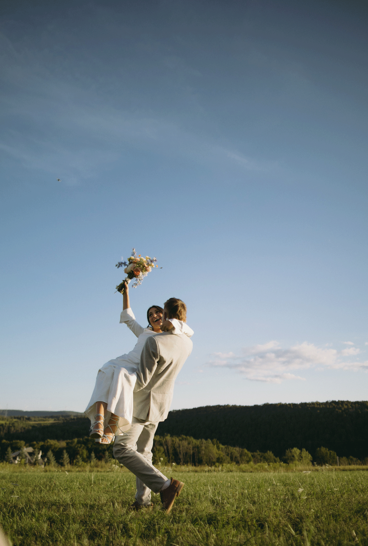 The groom spins his bride as she waves her bouquet with excitement.