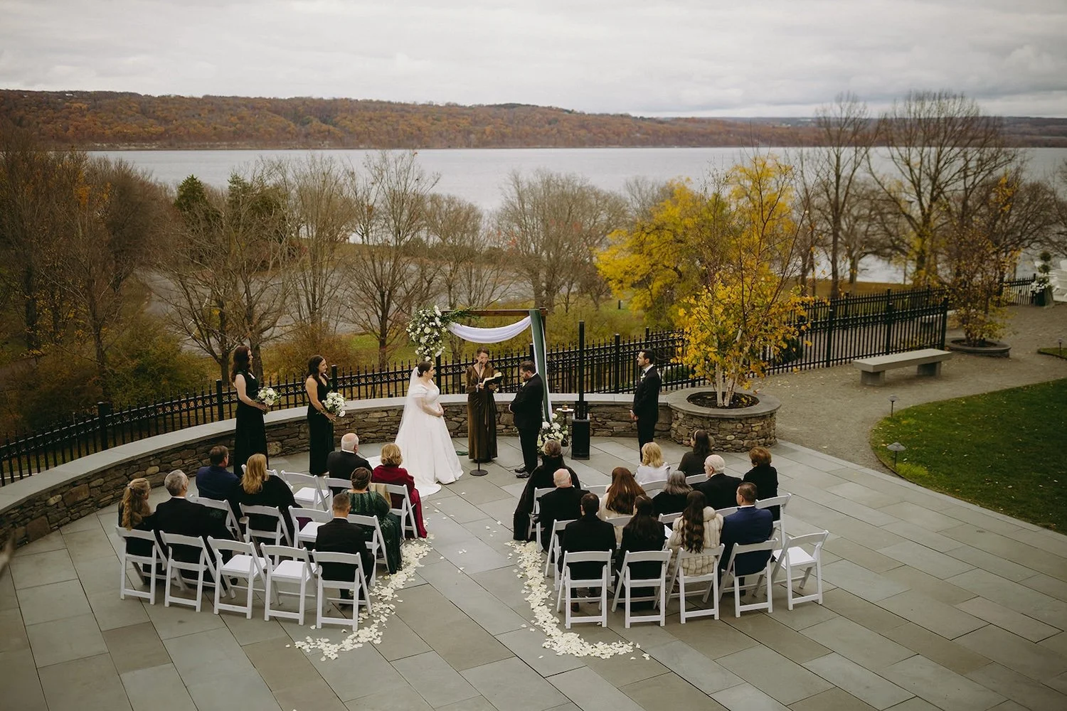 A distant photo of a wedding ceremony with guests and a view of the lake.