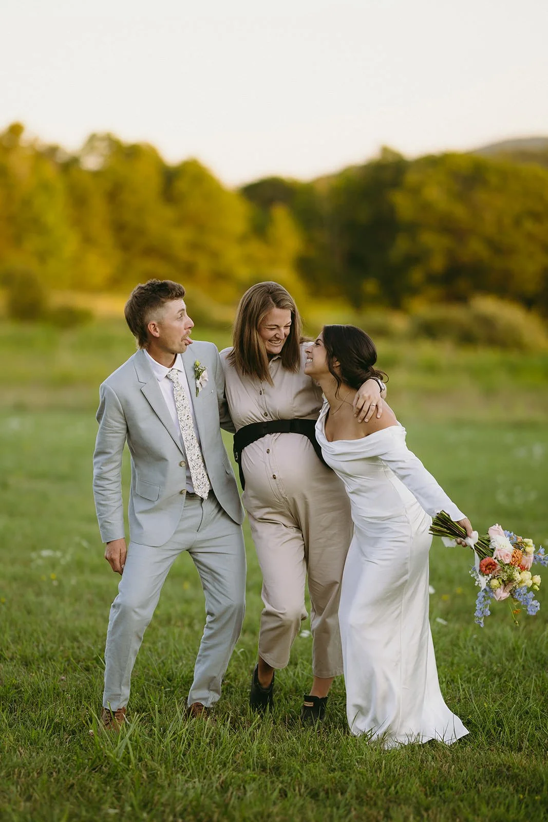Wedding photographer walking and laughing with a bride and groom in a grassy field, candid and fun wedding day storytelling.