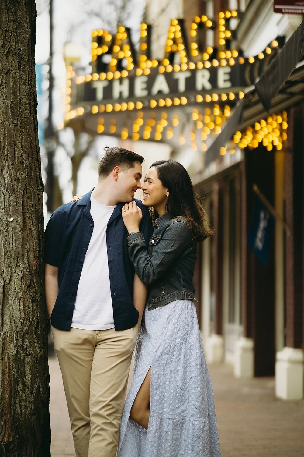 The happy couple lean against a tree with The Palace Theatre lit up above them.