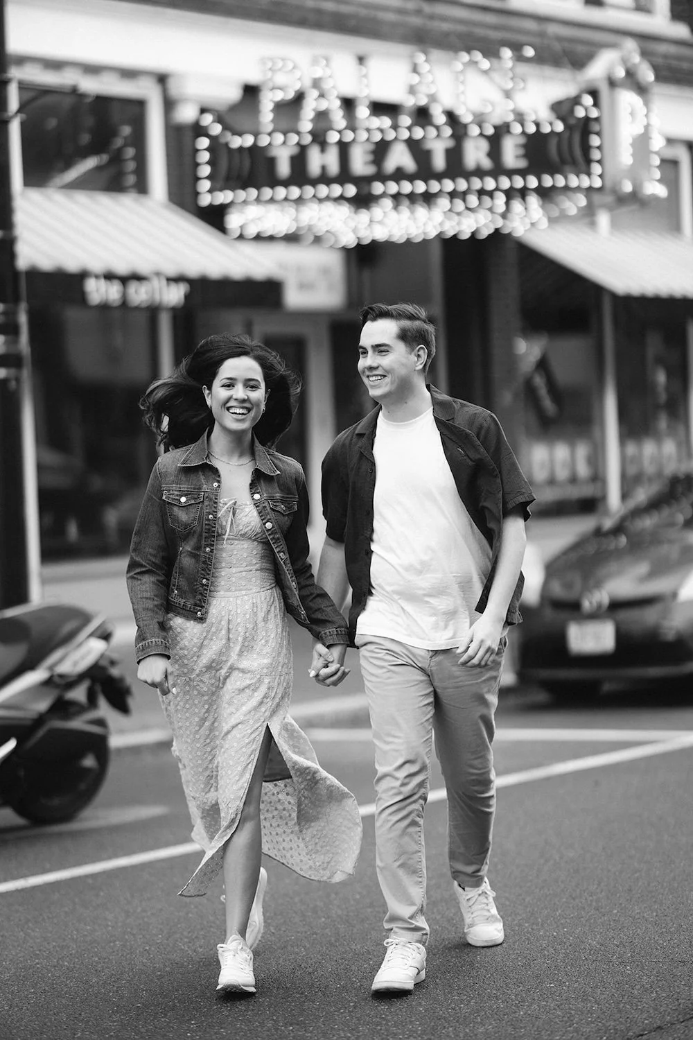 Black and white photo of the couple crossing the street hand in hand with smiles on their faces.