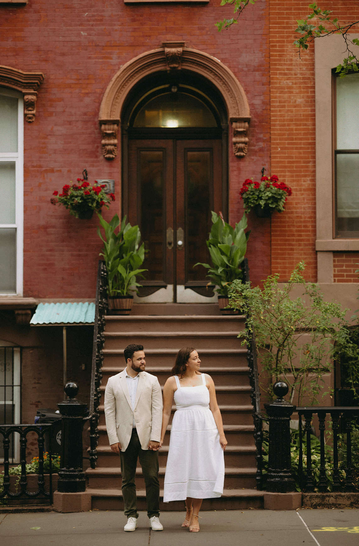 Couple standing infront of a brownstone building as the future bride fans her dress.