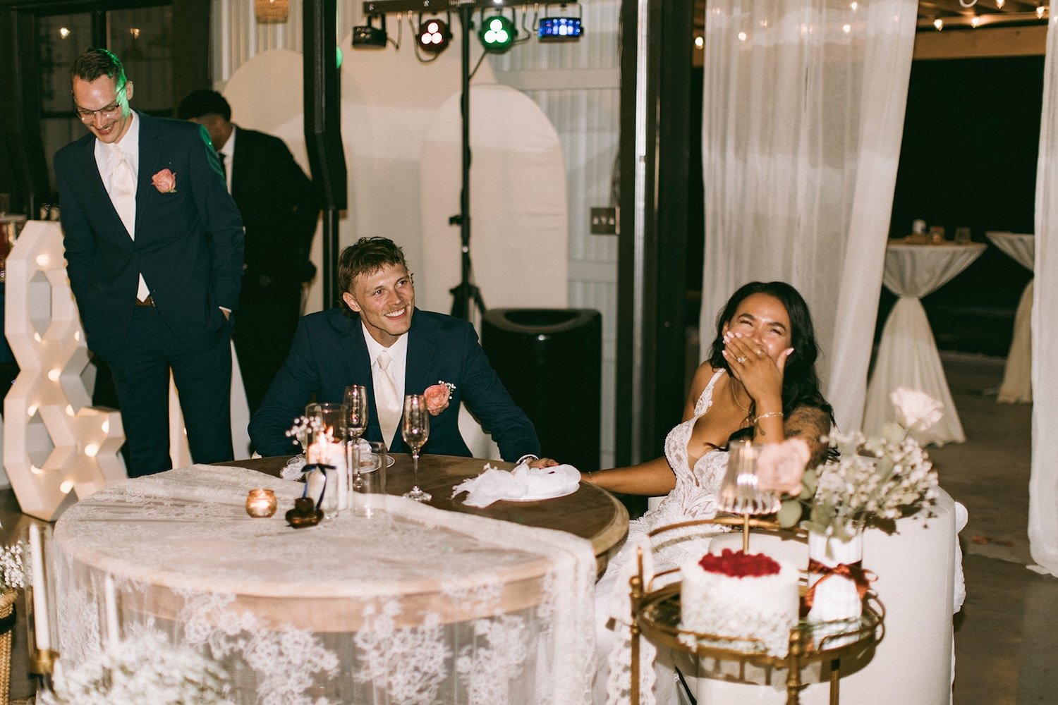 The bride and groom share a laugh at their head table while listening to speeches.