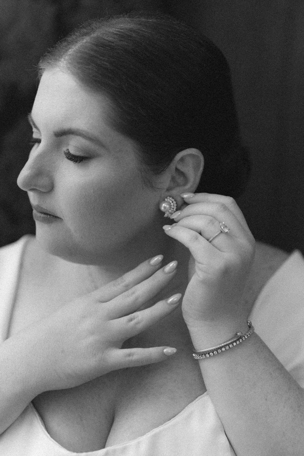 Black and white close up photo of the bride as she puts on her wedding earrings.