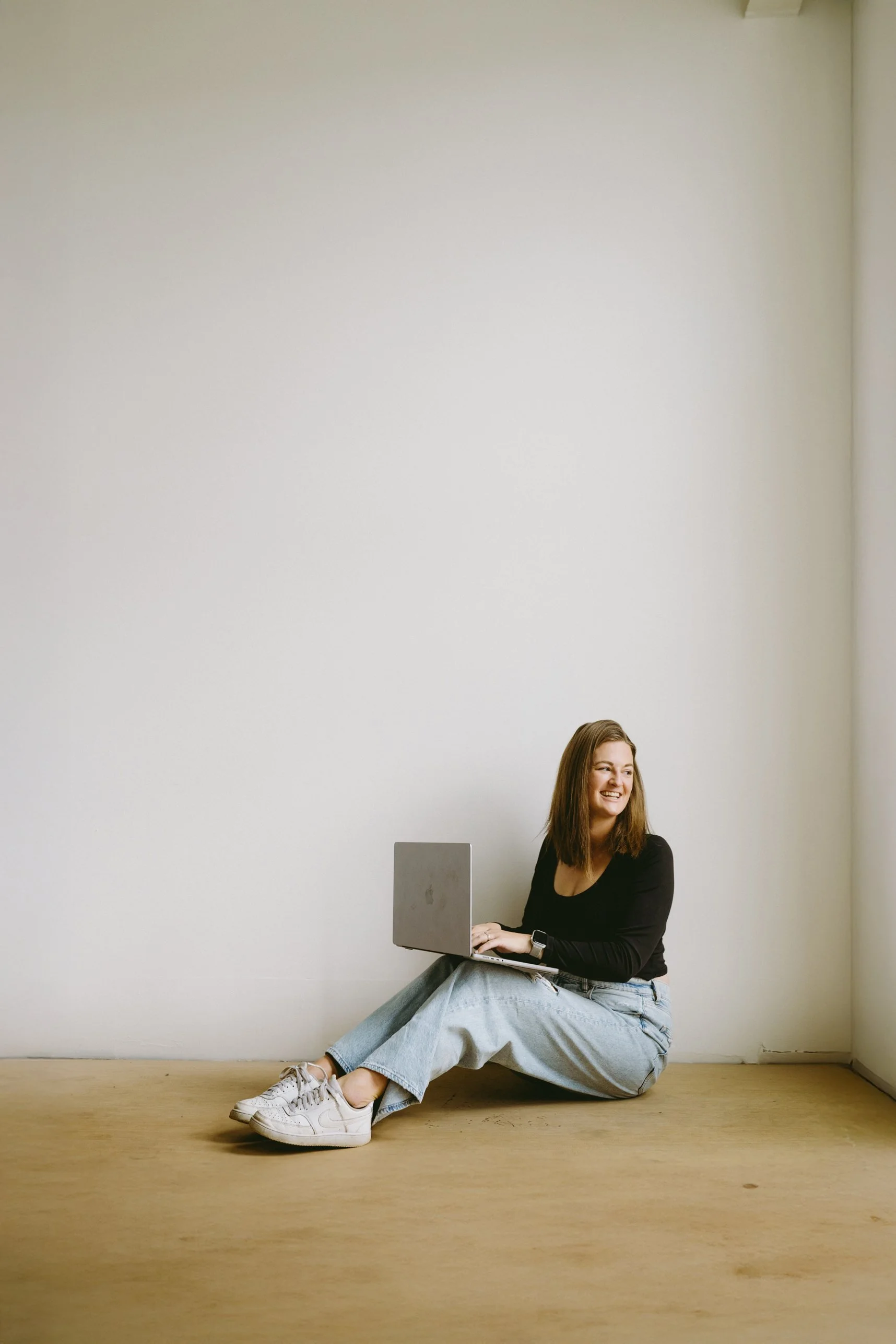 Lifestyle branding portrait of a wedding photographer sitting on the floor with a laptop, relaxed and approachable creative entrepreneur aesthetic.