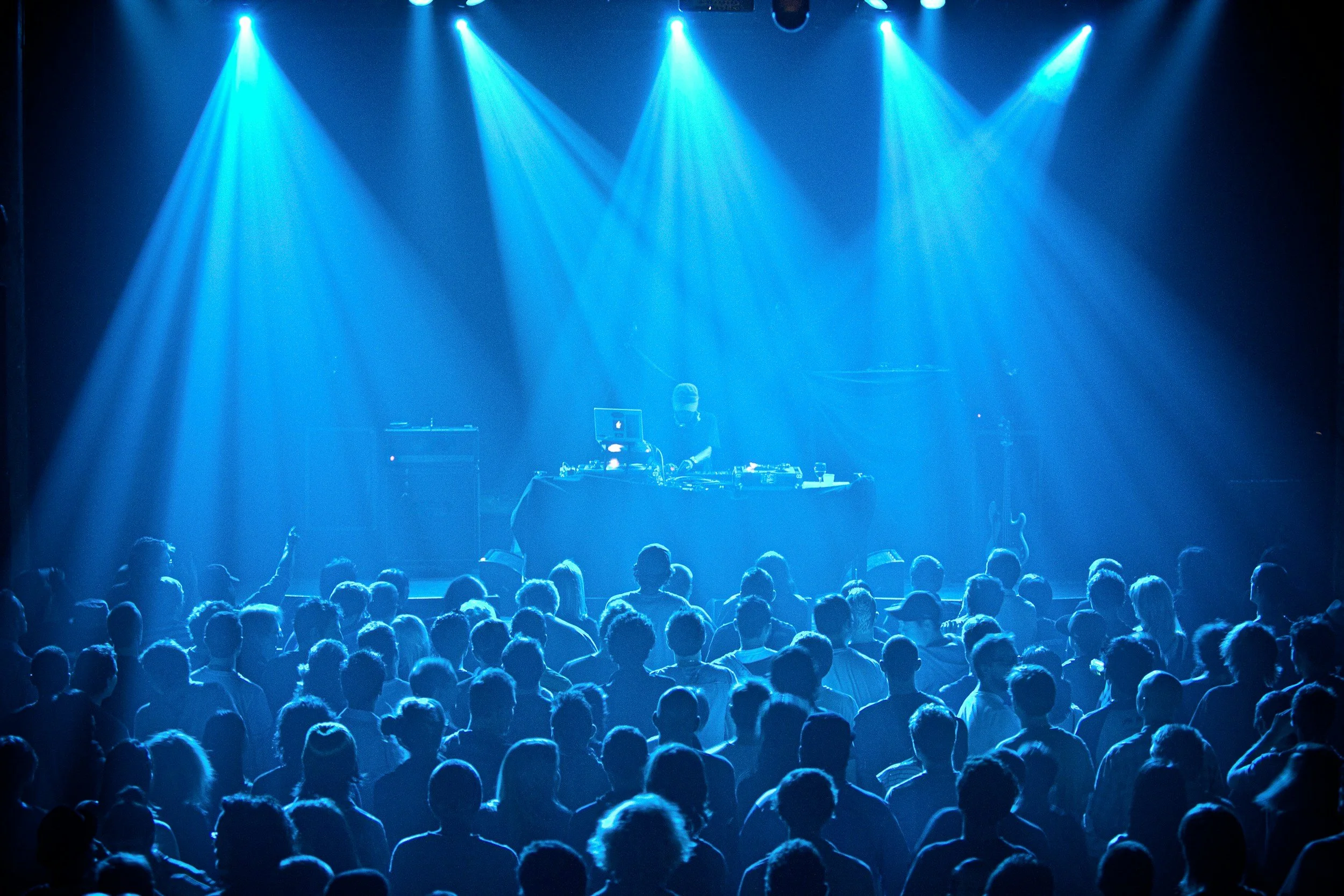 DJ performing on stage with a crowd under blue lights.