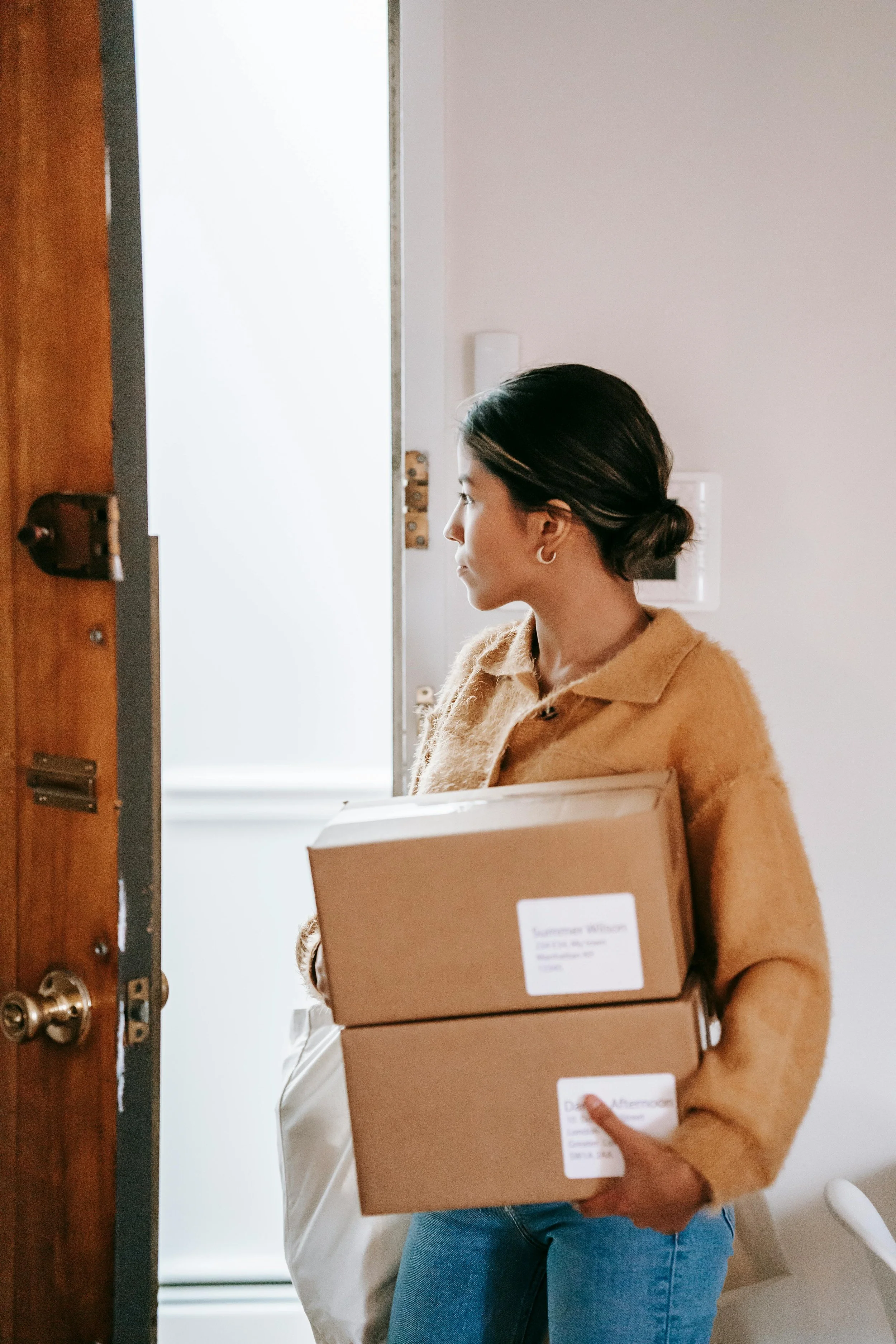 Young woman carrying moving boxes as she steps through the doorway of a new apartment, beginning a new chapter of independent living.