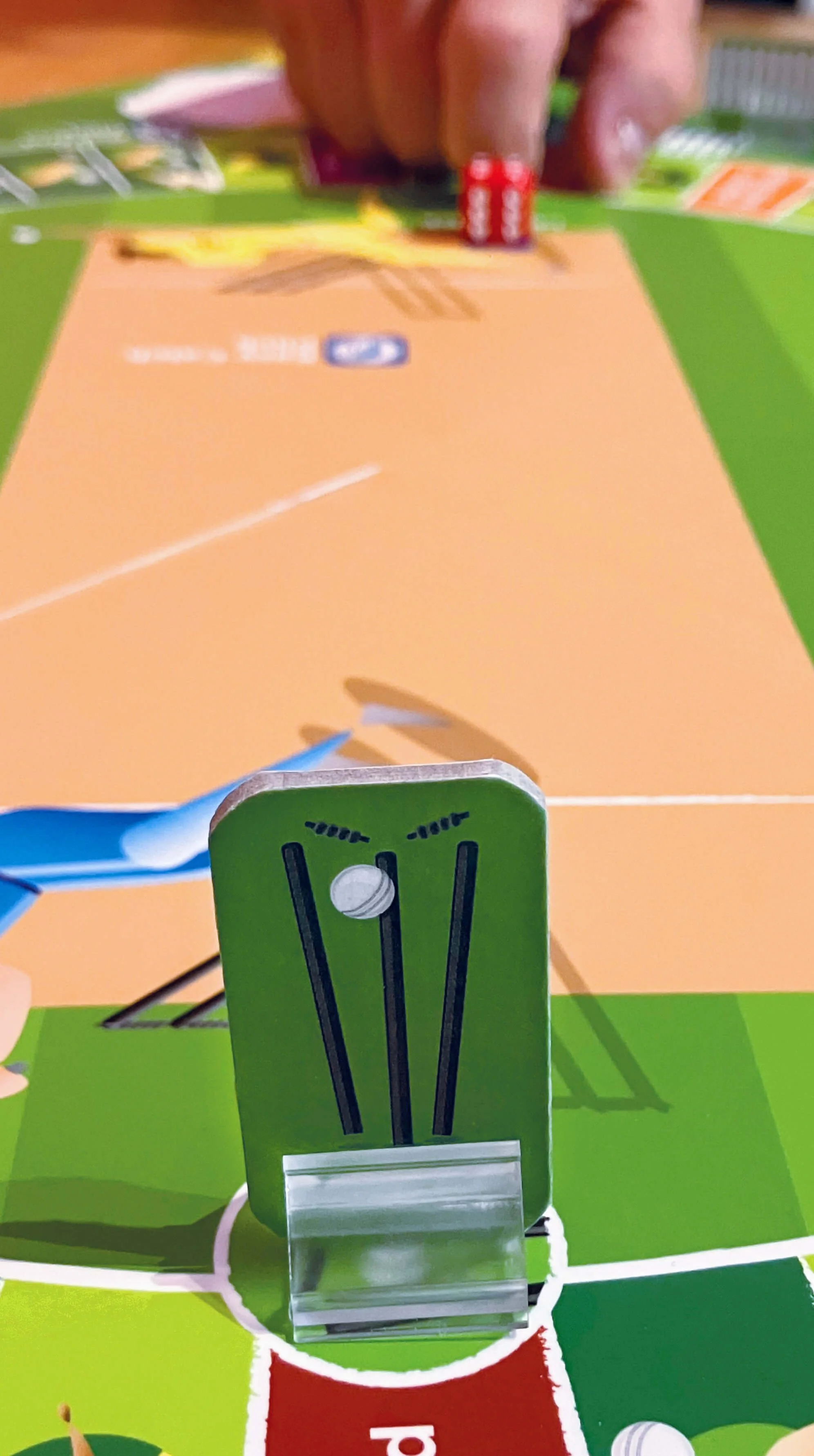 Close up of a cricket stumps target with a hand ready to flick a dice at the stumps.