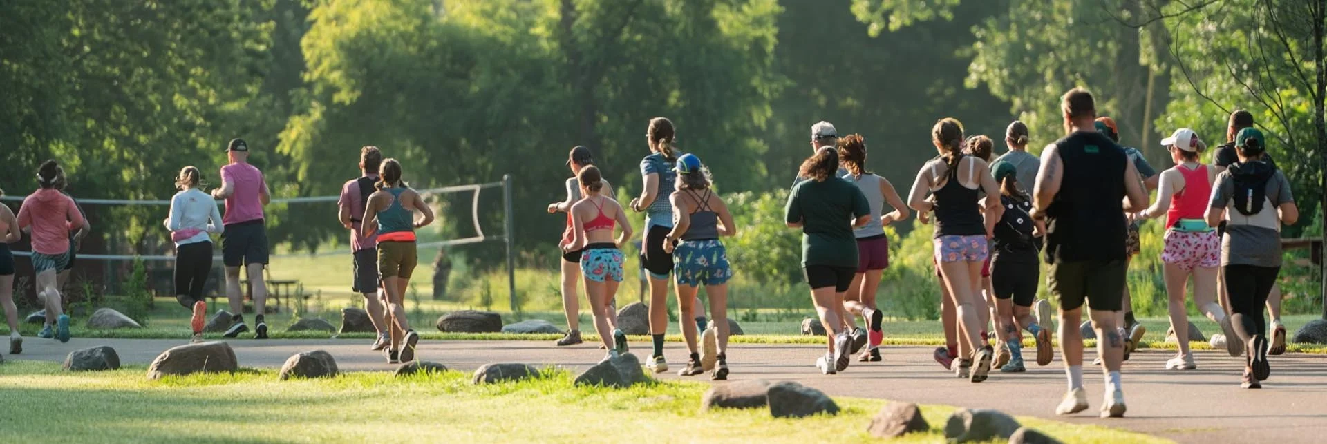 Group of people running outdoors on a paved trail in a park with green trees and grass.