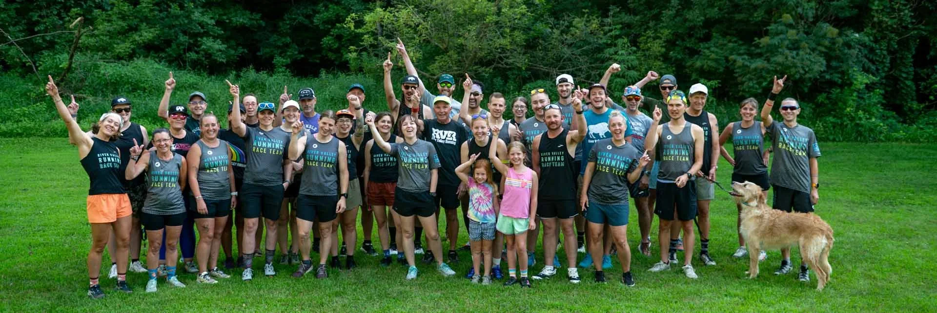 Group of people outdoors, in a grassy area surrounded by trees.