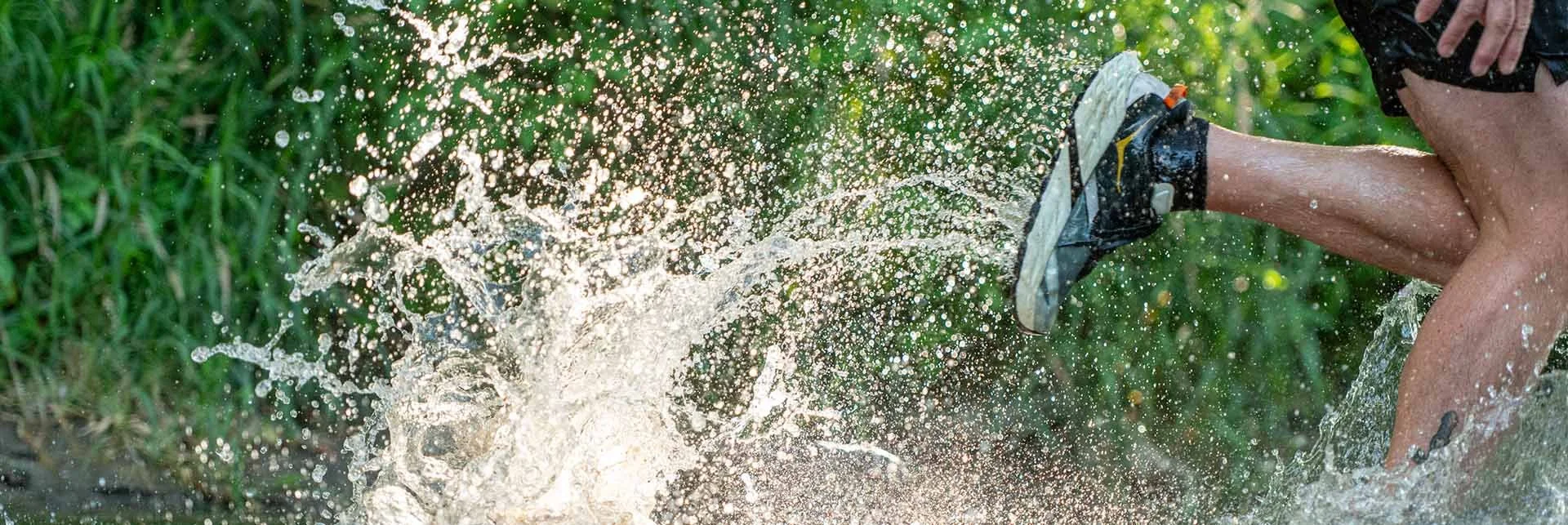Person wearing running shoes splashing water in a lush green outdoor setting.
