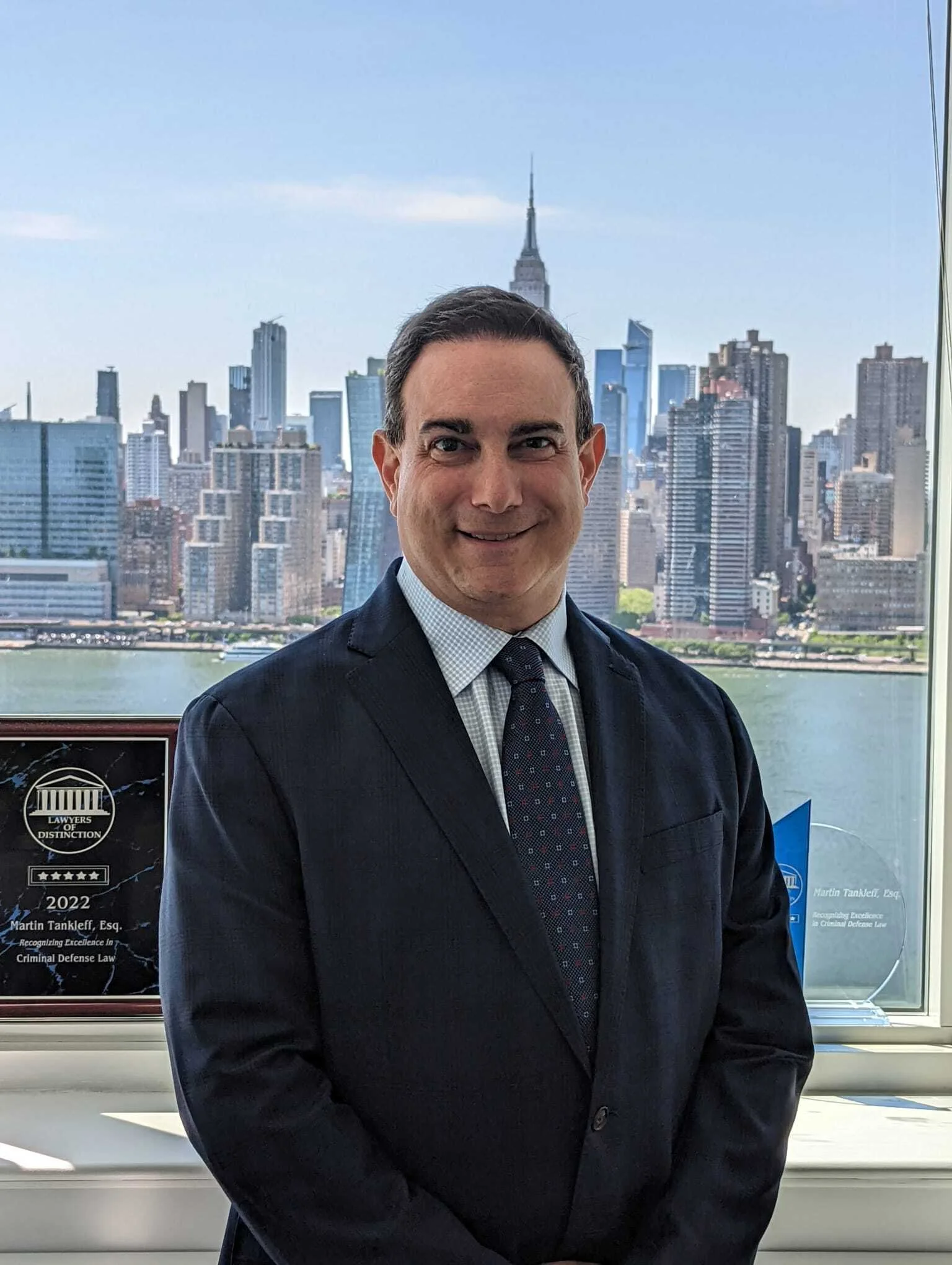 Black and white photo of a smiling man in business attire in front of a city skyline with tall buildings and a river.
