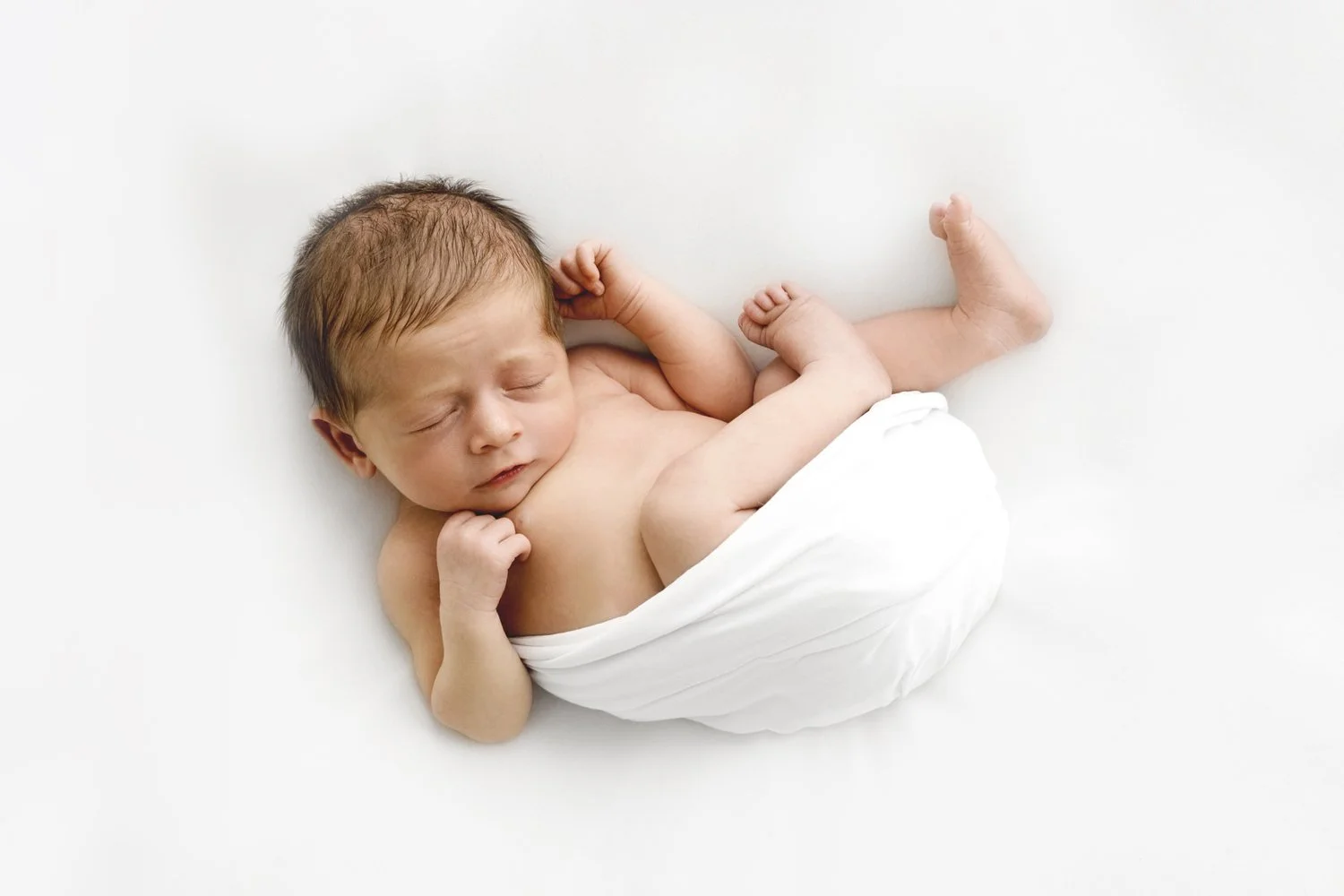 Sleeping newborn wrapped in soft white fabric in natural light at Dundee studio