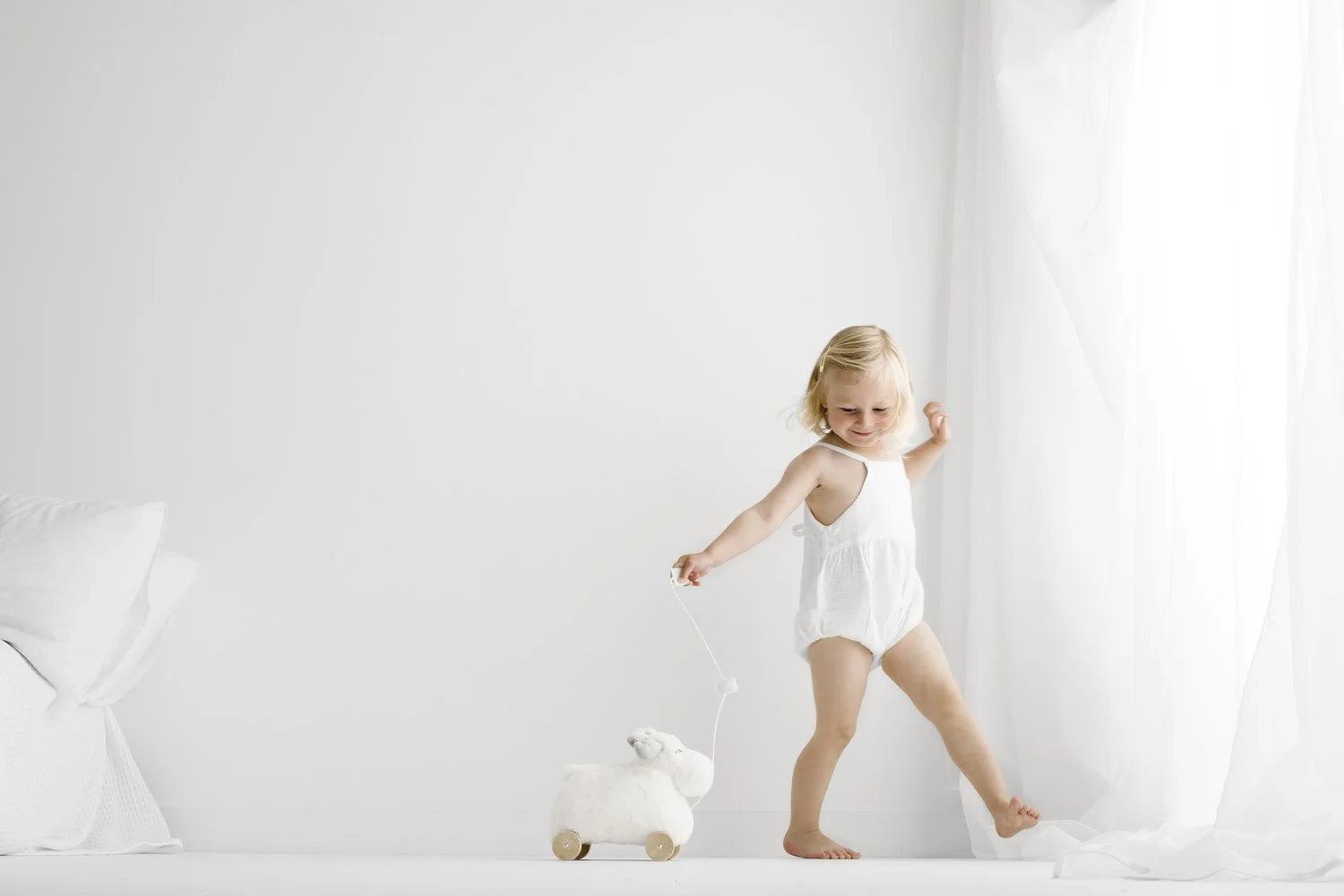 Toddler girl in white linen playsuit playing with wooden toy during newborn and sibling photoshoot in Dundee studio
