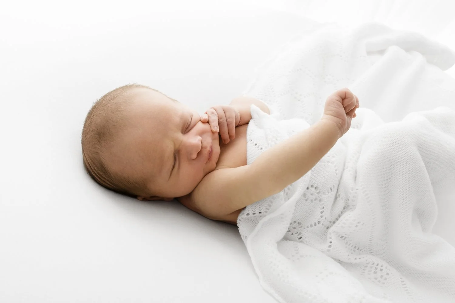 newborn baby in a white shawl stretching their arm and wriggling