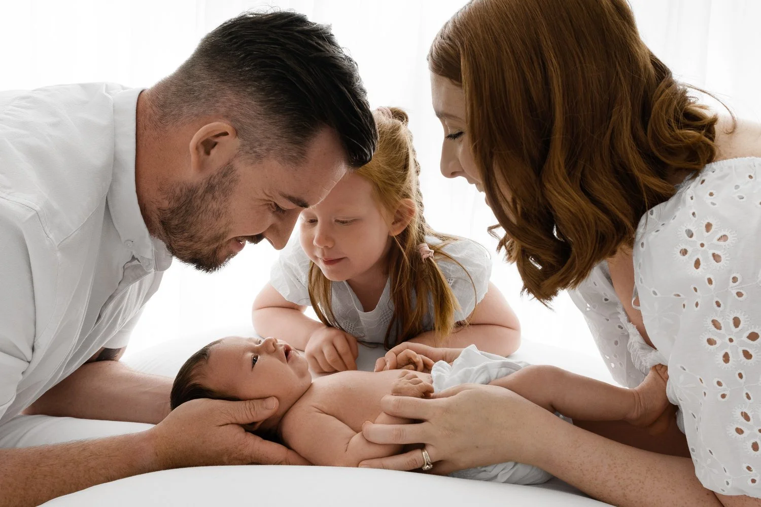 Parents and sibling looking down at their 3 week old newborn during natural Dundee studio photoshoot