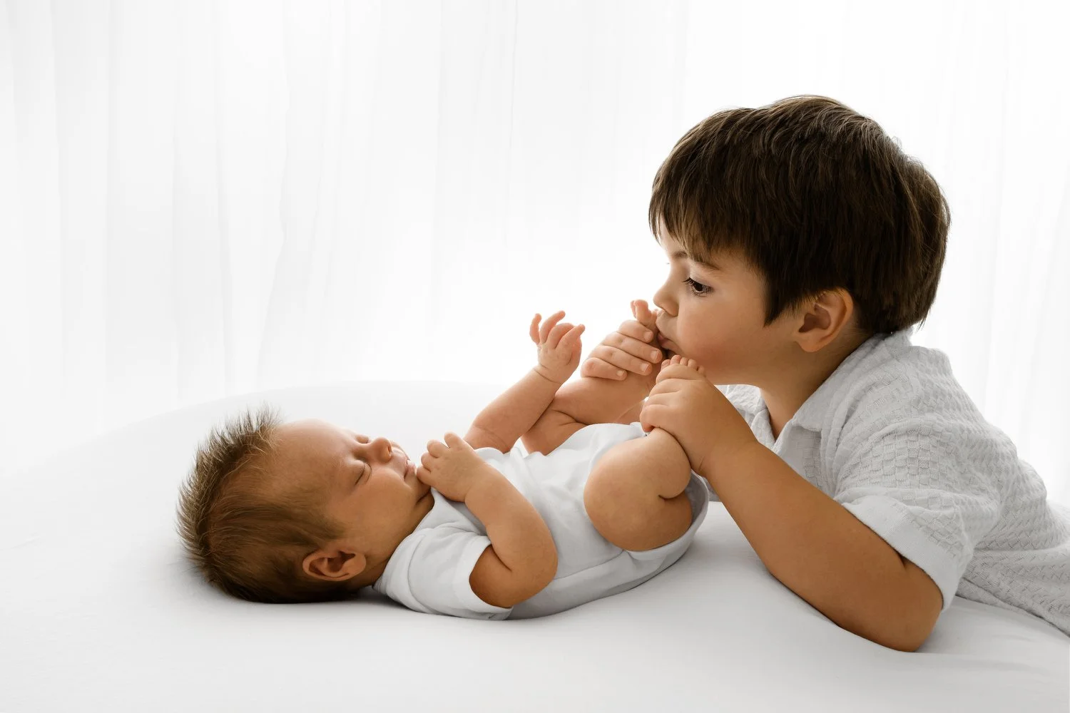 Toddler sibling kissing newborn baby toes during studio photoshoot in Dundee