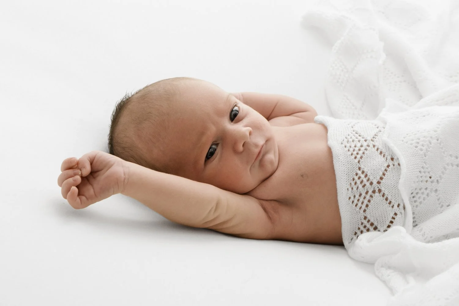 Awake newborn baby lying on side wrapped in white shawl at Mabel and Møøse newborn photography studio Dundee