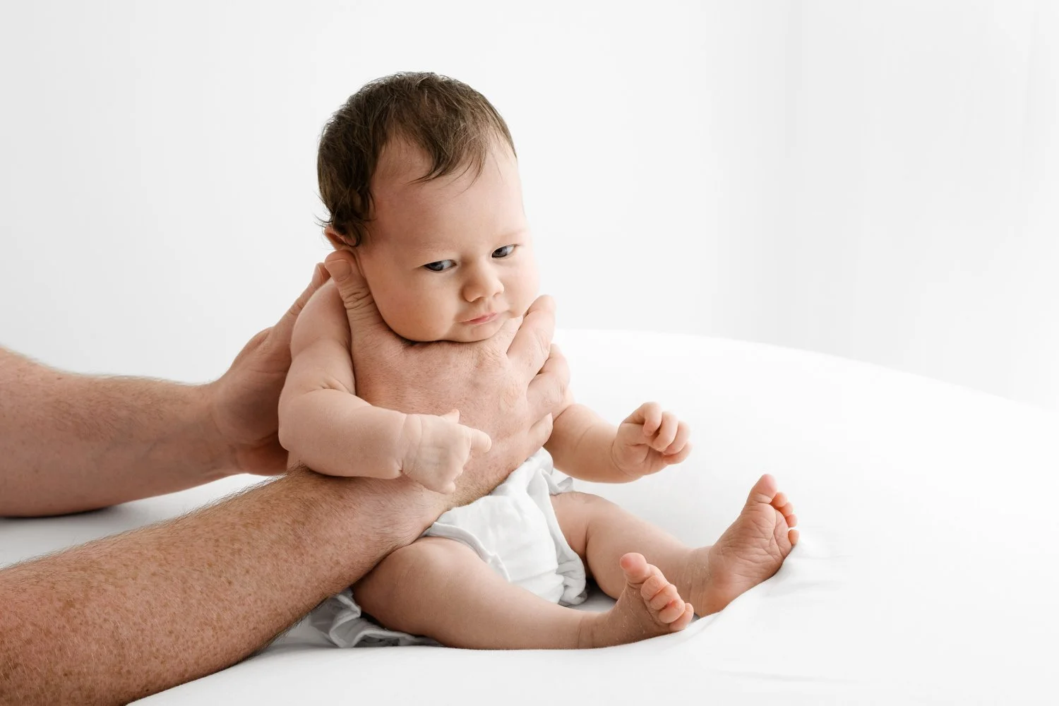 Awake 3 week old baby held upright in parent’s arms during natural studio photoshoot
