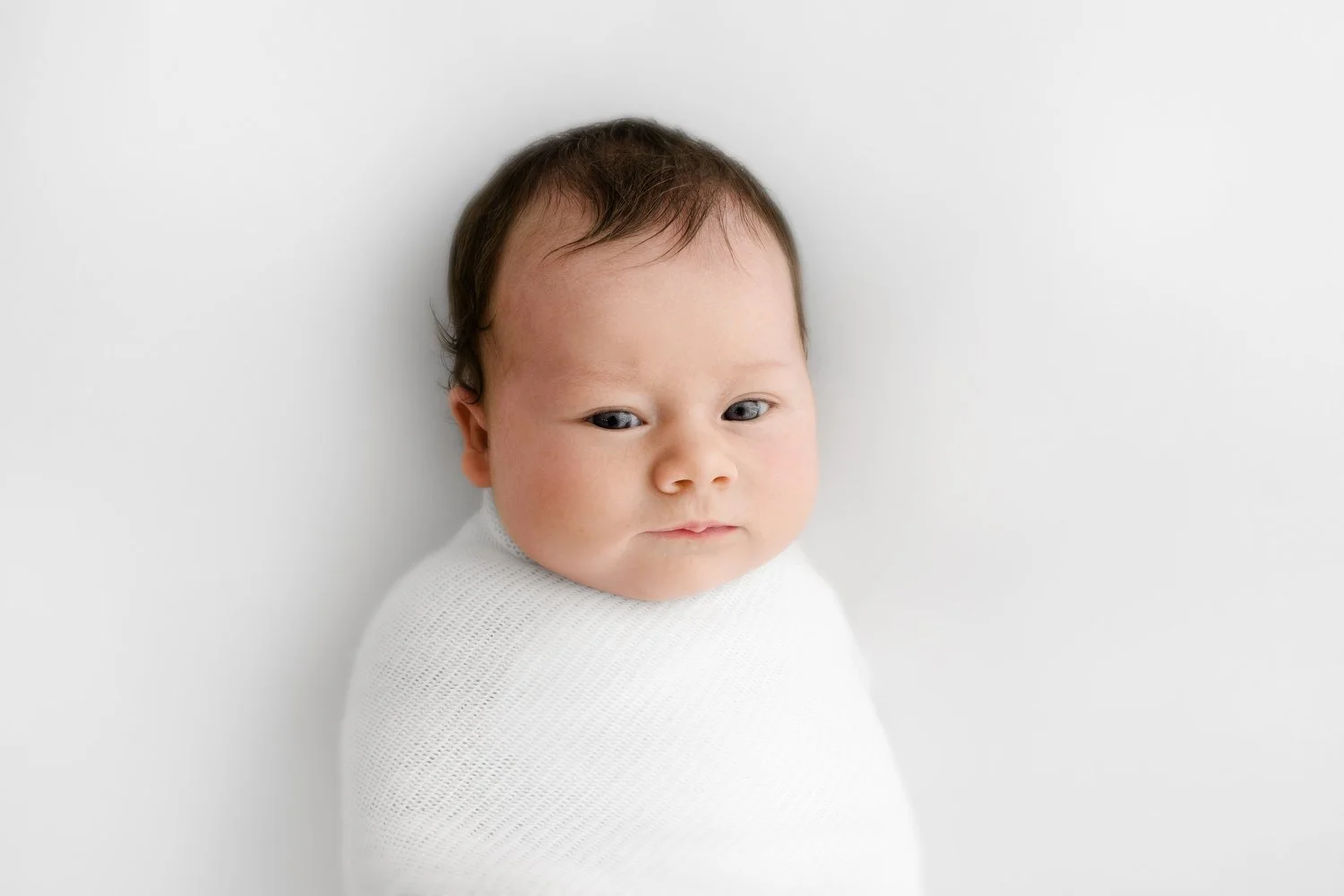 Awake 3 week old newborn wrapped in white blanket during Dundee photoshoot