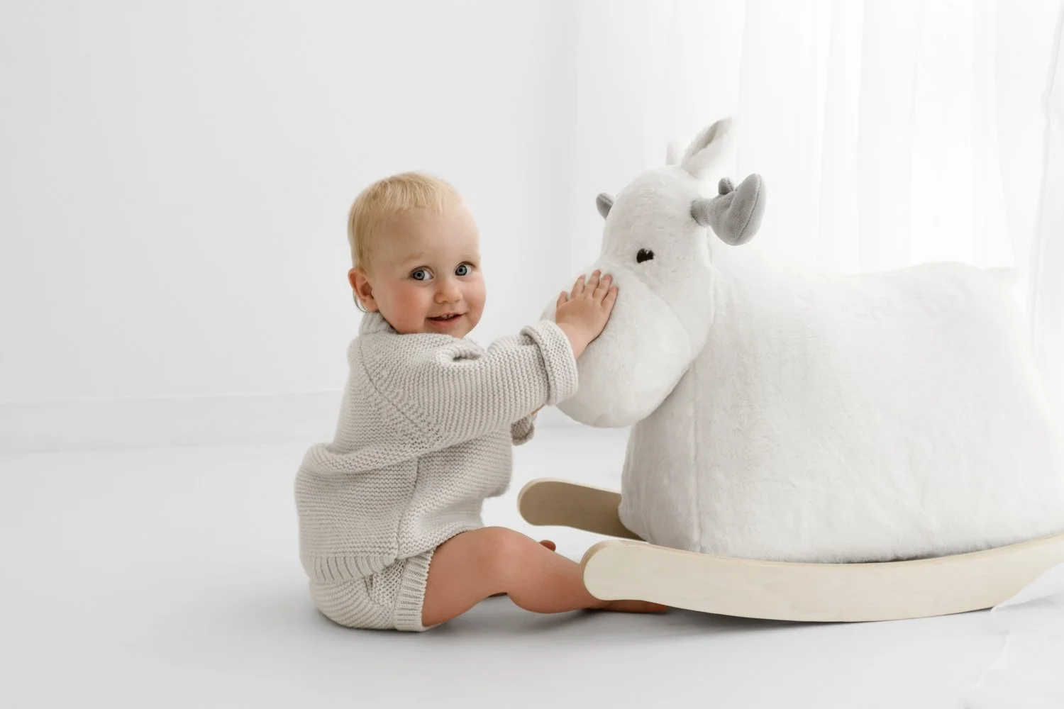 Baby sitting beside a white sit-on moose for their first birthday photoshoot in broughty ferry
