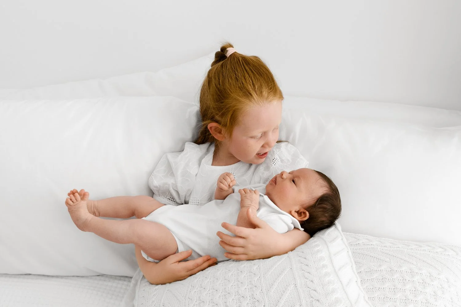 Young child in white outfit sitting beside newborn baby at Mabel and Moose photography studio Dundee