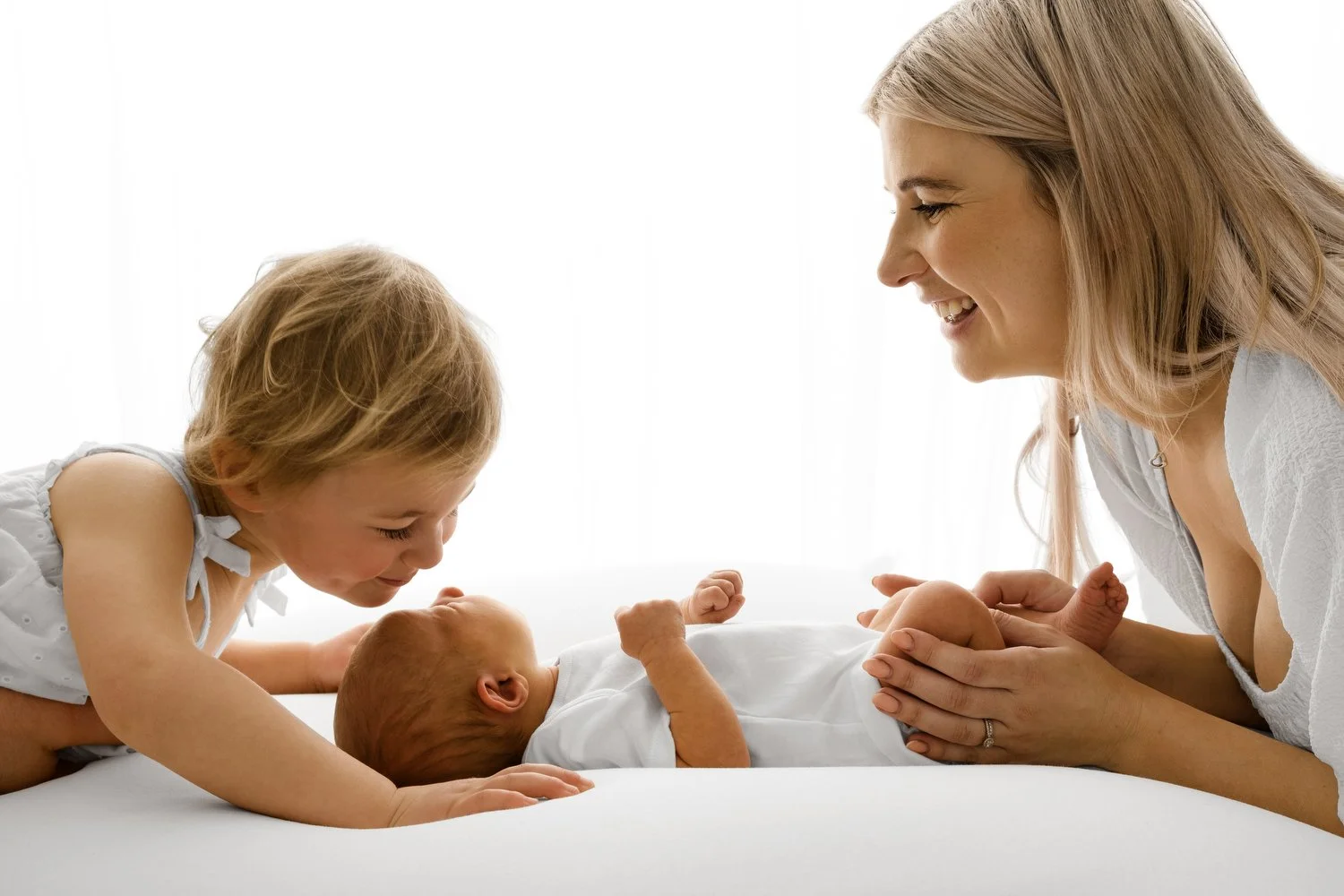 Mum and sibling looking at newborn baby on white beanbag at Mabel and Møøse newborn photography studio Dundee