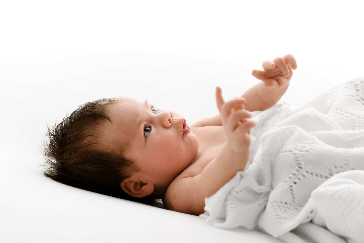 Newborn baby girl wrapped in a white lace shawl, posed simply on a soft neutral background to illustrate calm, timeless newborn photography.