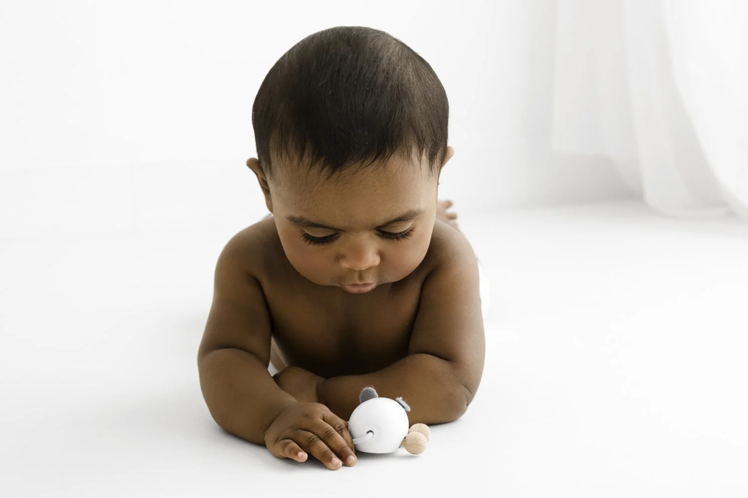 Older baby lying on tummy playing with wooden toy during Dundee studio photoshoot