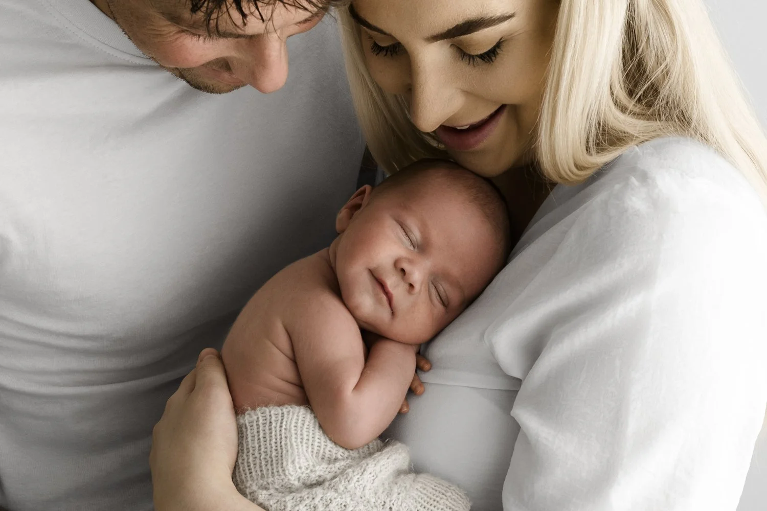 natural photo of mum and dad snuggling their newborn baby who is sleeping. uncluttered style