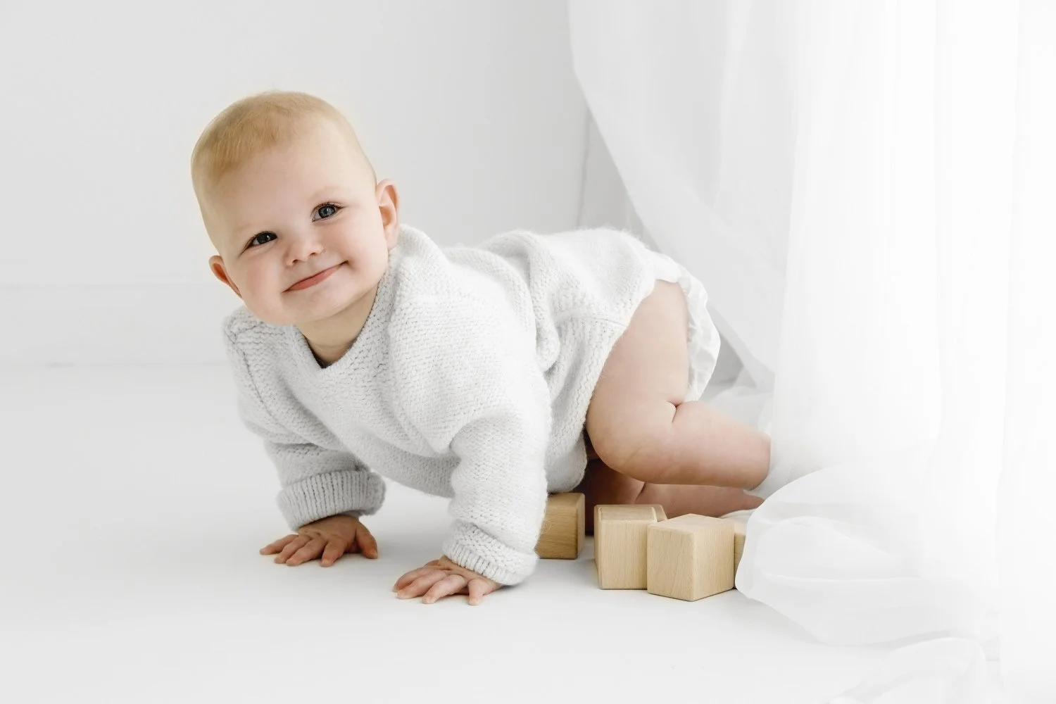 8 month baby crawling on a white background wears a neutral knitted jumper