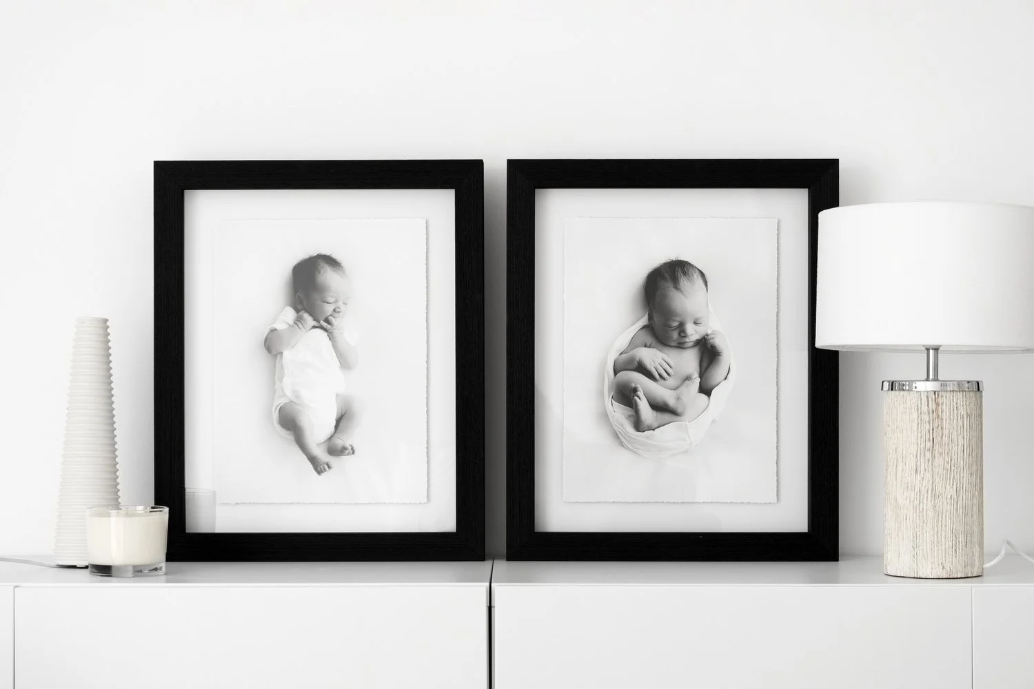 Two black framed black and white newborn portraits displayed on a white sideboard