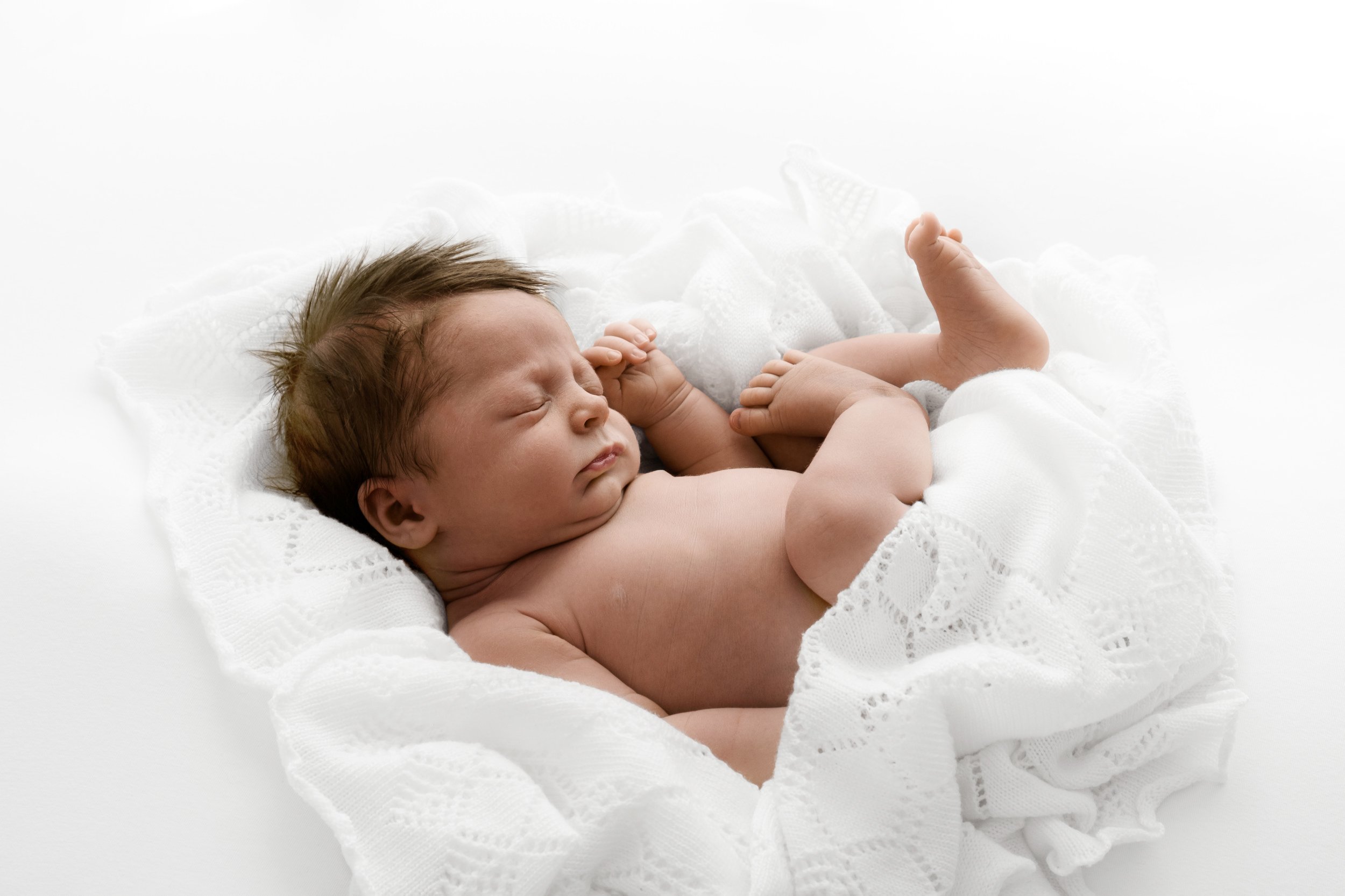 Sleeping newborn on white blanket in natural pose at Dundee studio