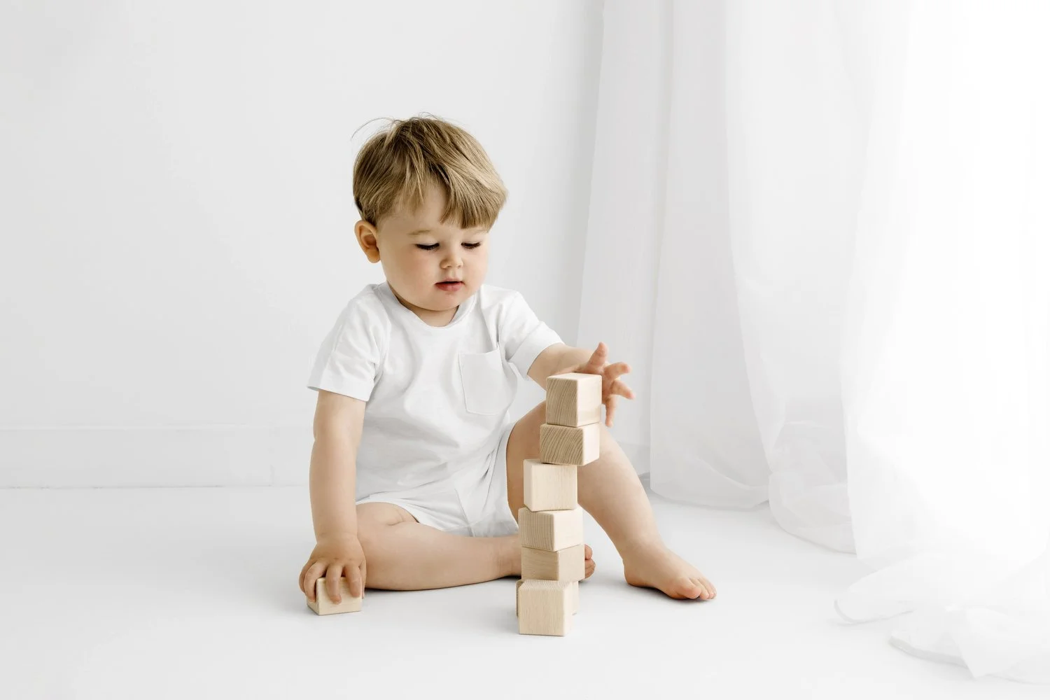 Toddler sibling playing with wooden toy during newborn and sibling photoshoot in Dundee studio