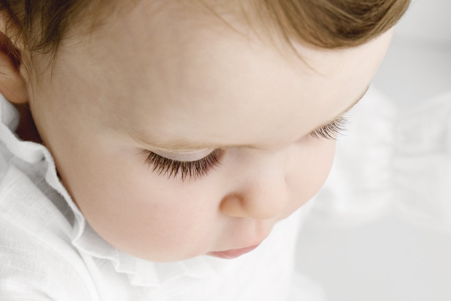 close up of 9 month old baby with dark eye lashes and white linen romper