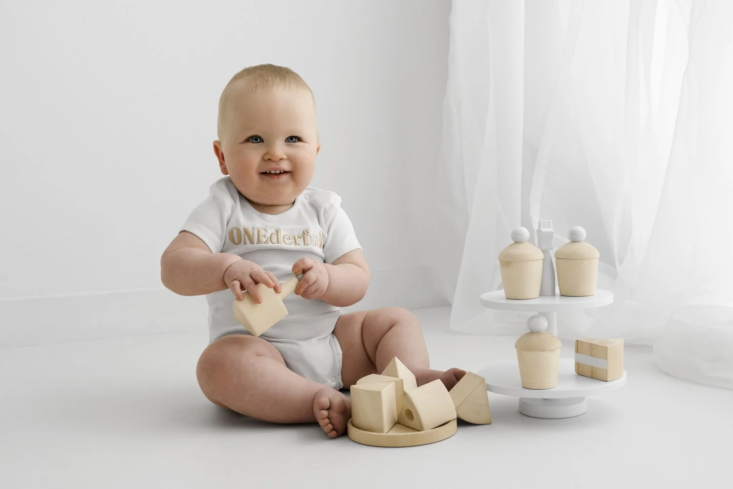 12 month baby with wooden first birthday cake wearingonederful white vest