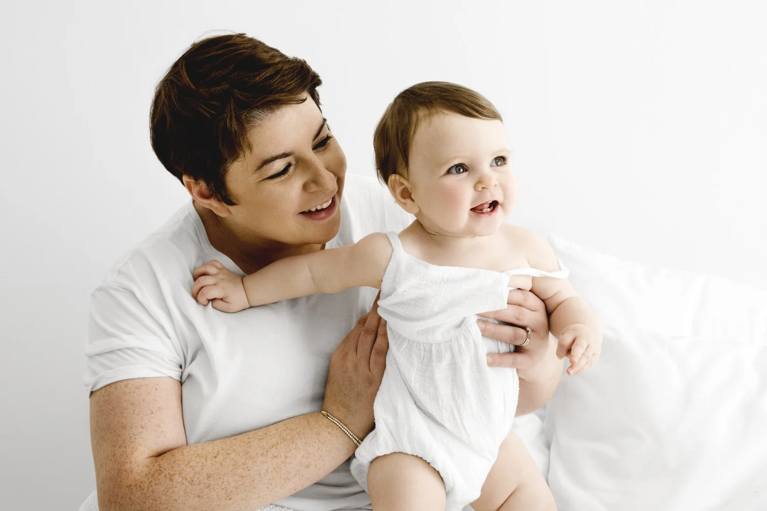 mum looking at 9 month old baby in white romper in natural studio session