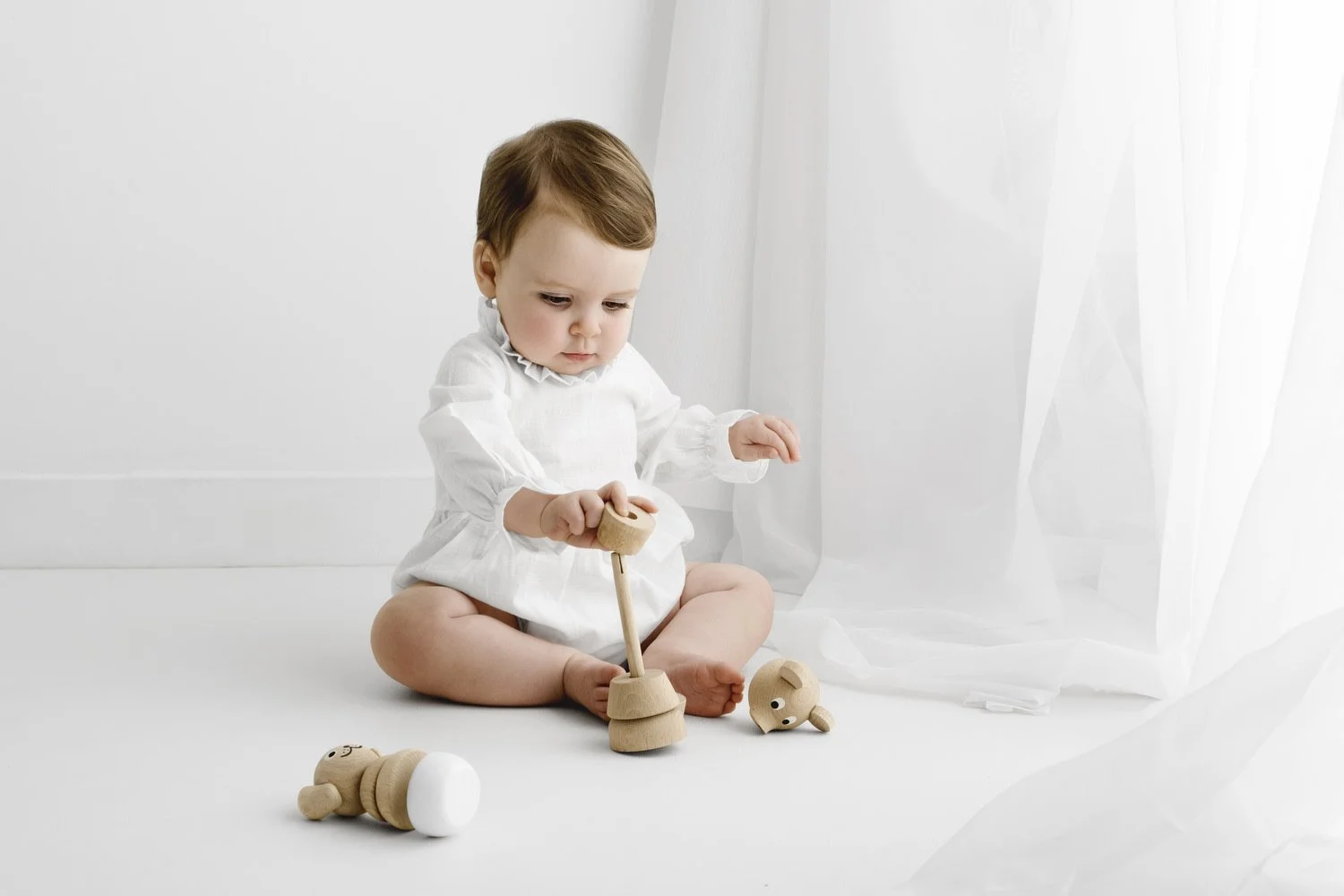 9 month old baby playing with natural wooden toys in white studio session