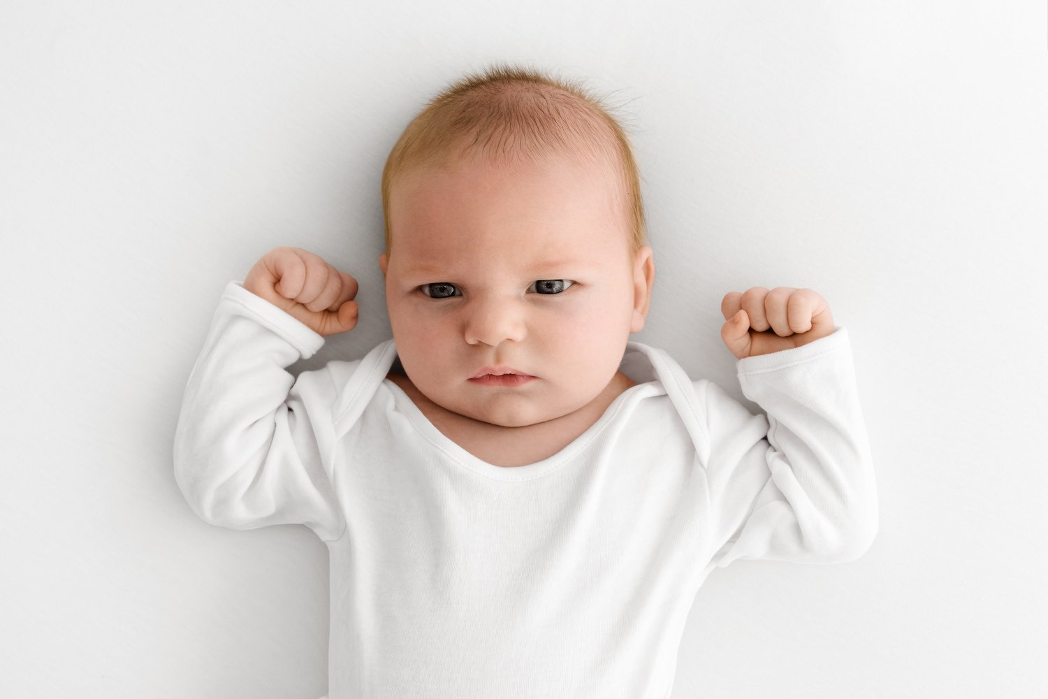 Awake baby with wide bright eyes lying comfortably on a neutral studio backdrop